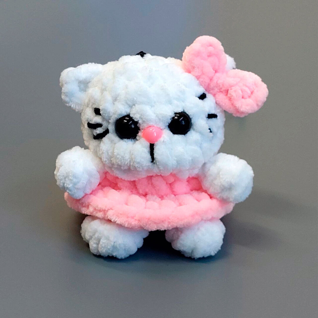 A cute crocheted amigurumi kitty cat keychain with a pink bow and skirt.